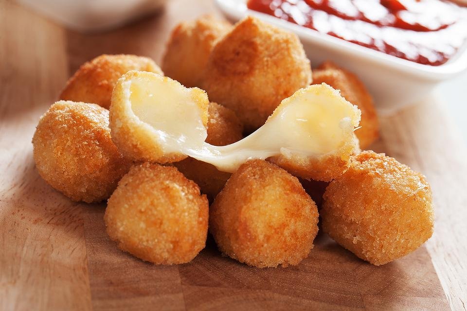 olden, crispy breaded cheese balls on a wooden board—one torn open with gooey cheese stretching out—perfect for birthday party catering services near me, served with a bowl of ketchup dip.