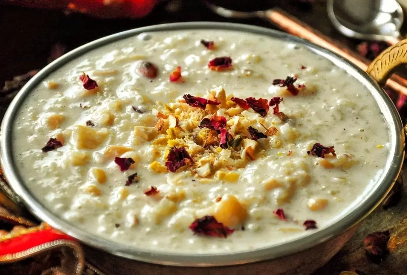 A close-up of creamy kheer garnished with chopped nuts and rose petals in a decorative brass bowl, beautifully presented by naming ceremony catering services near me in Bangalore.