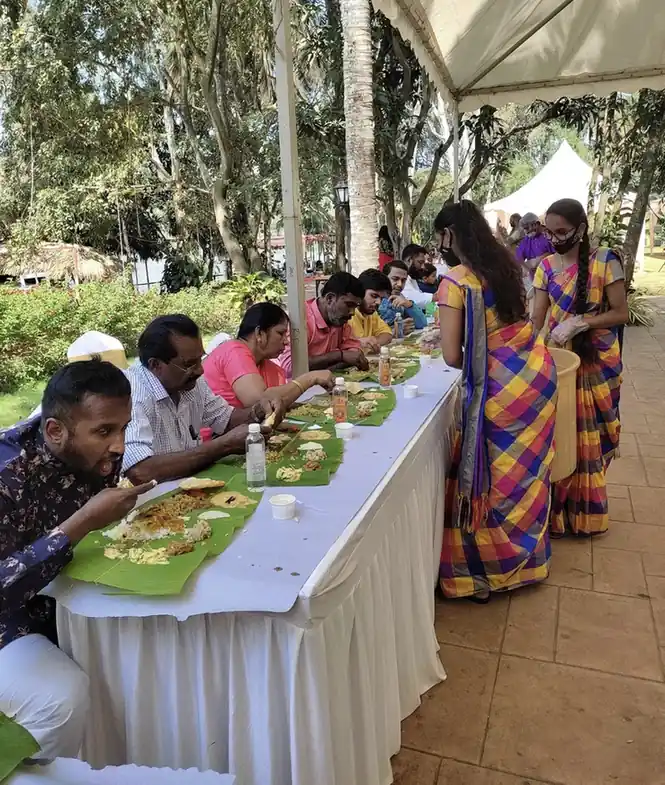 Caterers serving food to guests seated at long banana leaf dining tables