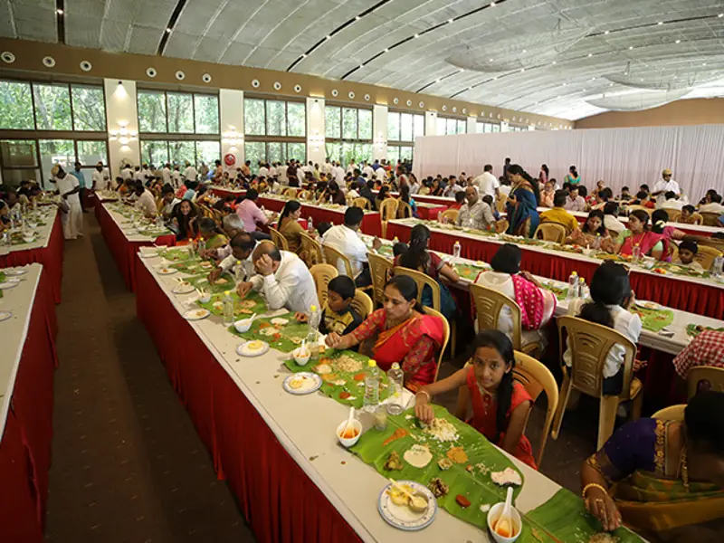 Large event hall food service with guests dining on banana leaves during a vegetarian catering event