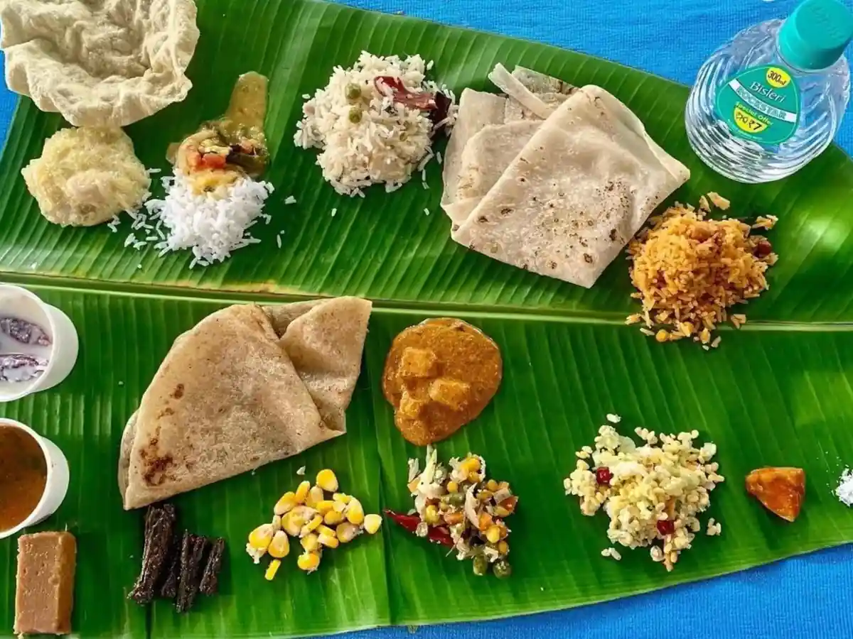 Traditional South Indian vegetarian lunch being served on a banana leaf with rice, sambar, curries, chutneys and papad