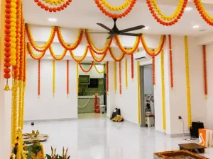 Housewarming hall decorated with yellow and orange flower garlands in Bangalore