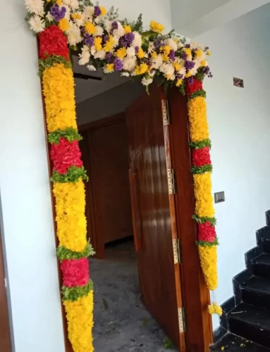 Fresh marigold and mixed flower decoration at apartment entrance for housewarming ceremony in Bangalore.
