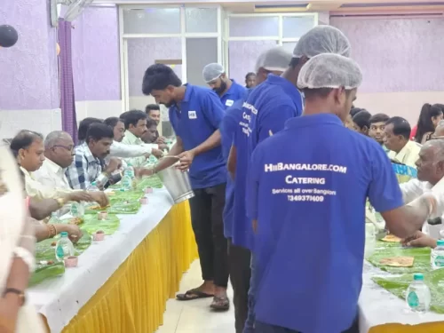 Professional catering staff serving food on banana leaves at a large vegetarian event
