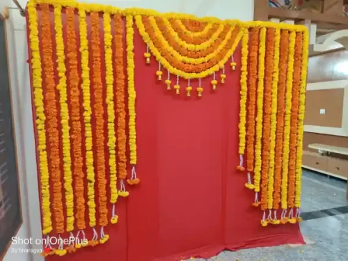 Traditional housewarming puja flower decoration with yellow and orange marigold garlands on red backdrop in Bangalore